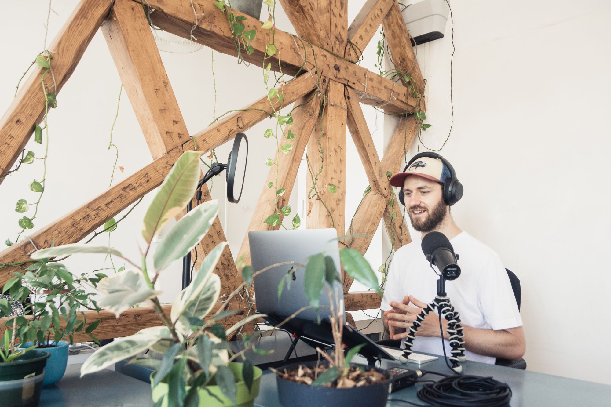 Un podcaster con cuffie e microfono in uno studio con travi e piante