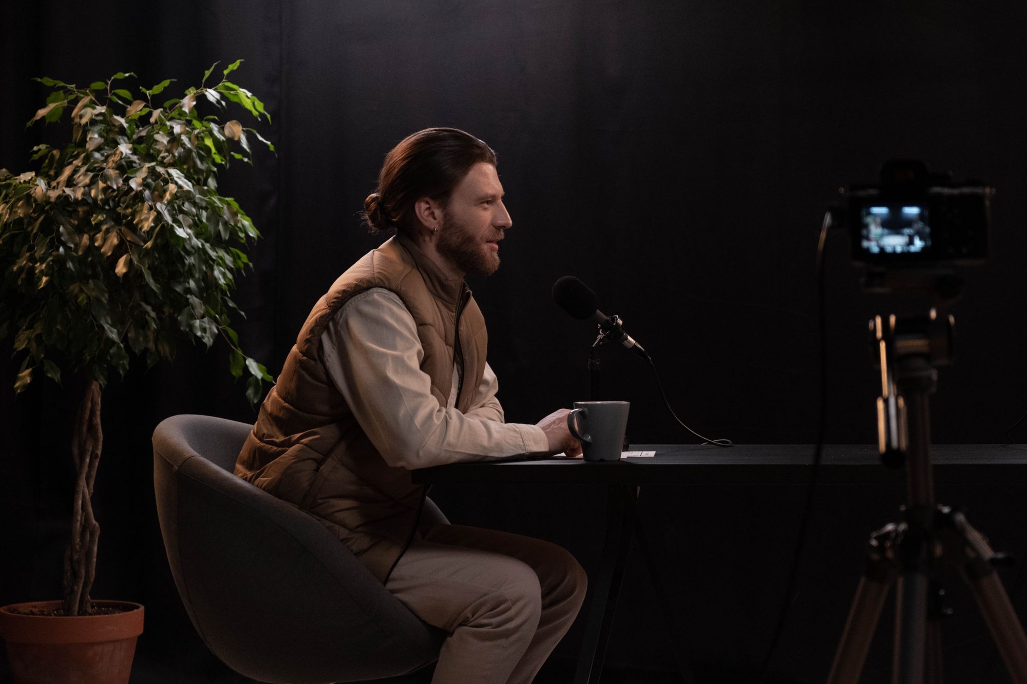 Un podcaster al tavolo con un microfono in uno studio scuro